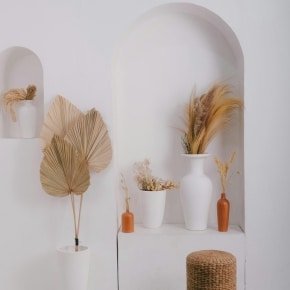 Décoration intérieure minimaliste avec objets artisanaux, vases blancs, feuillages secs et tabouret en fibres naturelles