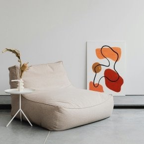 Fauteuil en tissu beige, table d'appoint blanche avec vase design et tableau moderne dans un intérieur épuré.