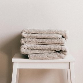 Pile de textiles en lin beige pliés sur un tabouret blanc dans un intérieur minimaliste et chaleureux.